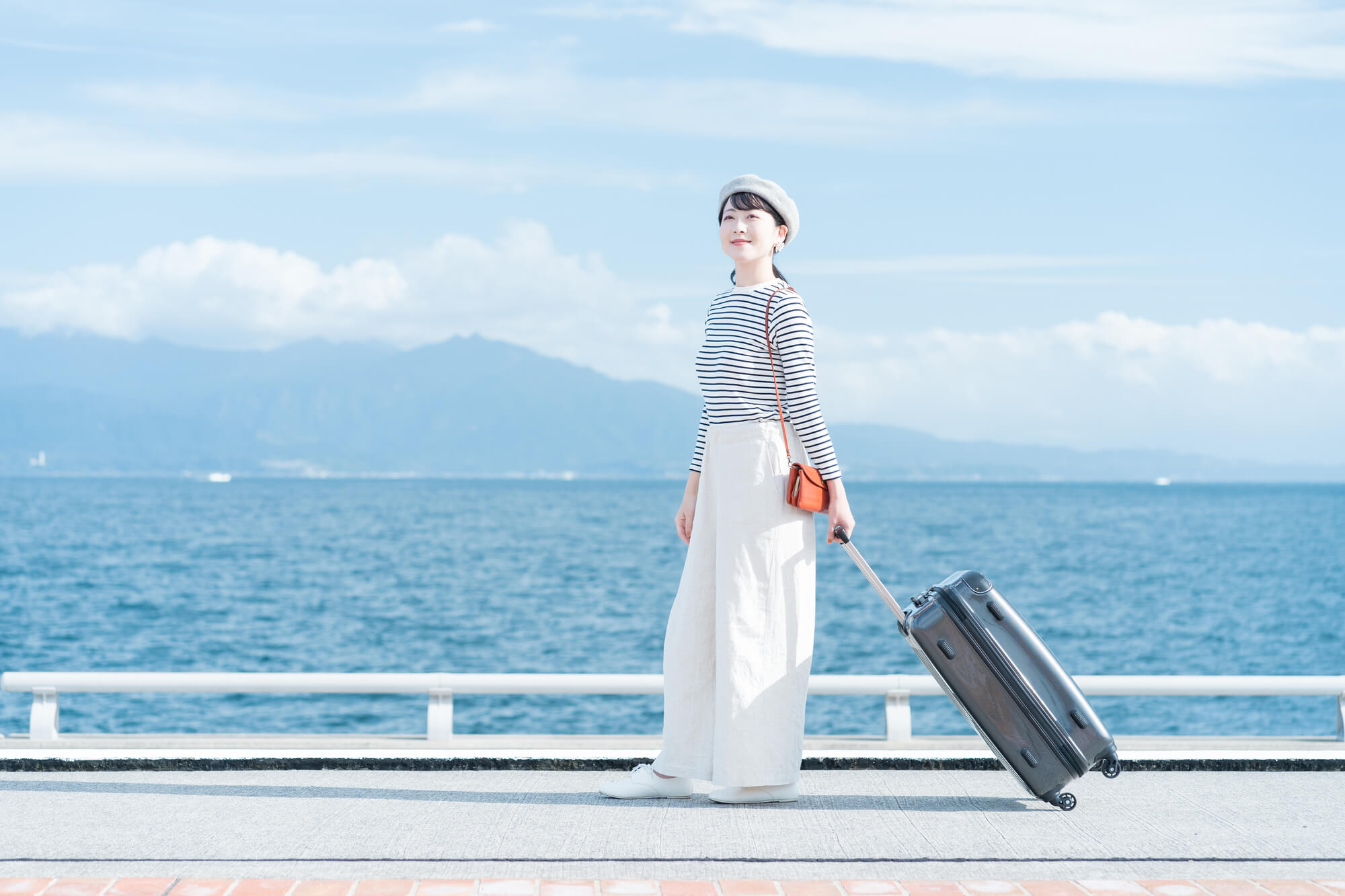 海辺をスーツケースを持って歩く女性